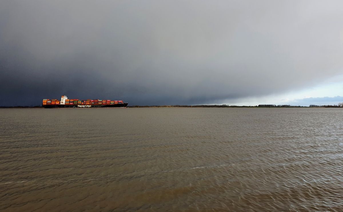 Containerschiff auf der Elbe Höhe Stade auf dem Weg nach Hamburg vor einem winterlichen Regenschauer