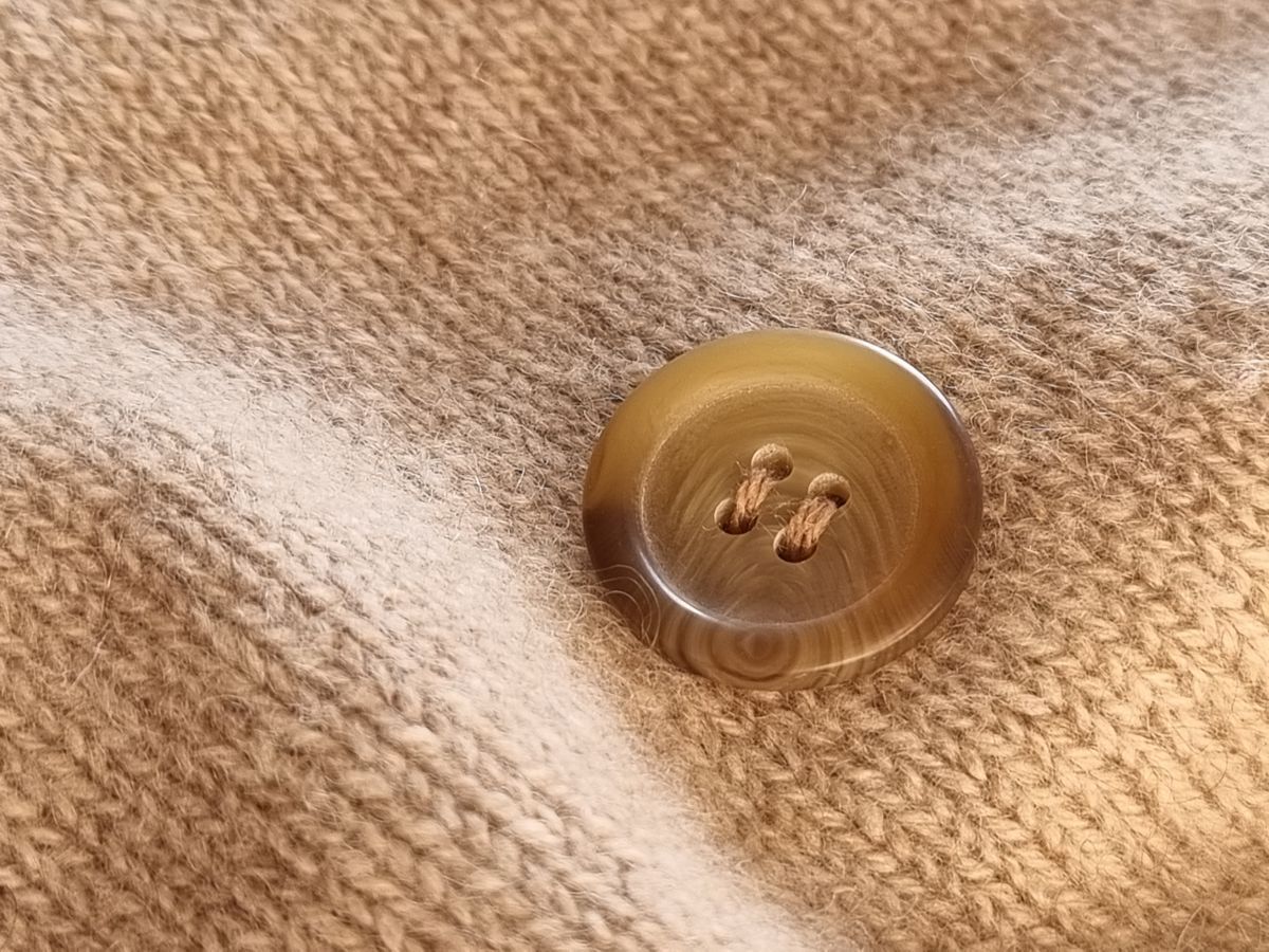 Ein gestopftes Loch in einem Kaschmirponcho lässt sich mit einem aufgenähten Knopf kaschieren.