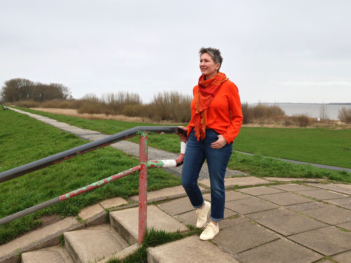 Ines Meyrose - Outfit 2023 - Jeans, Pullover Orange, Sneaker Creme, Dreieckstuch bunte Orange-Rottöne