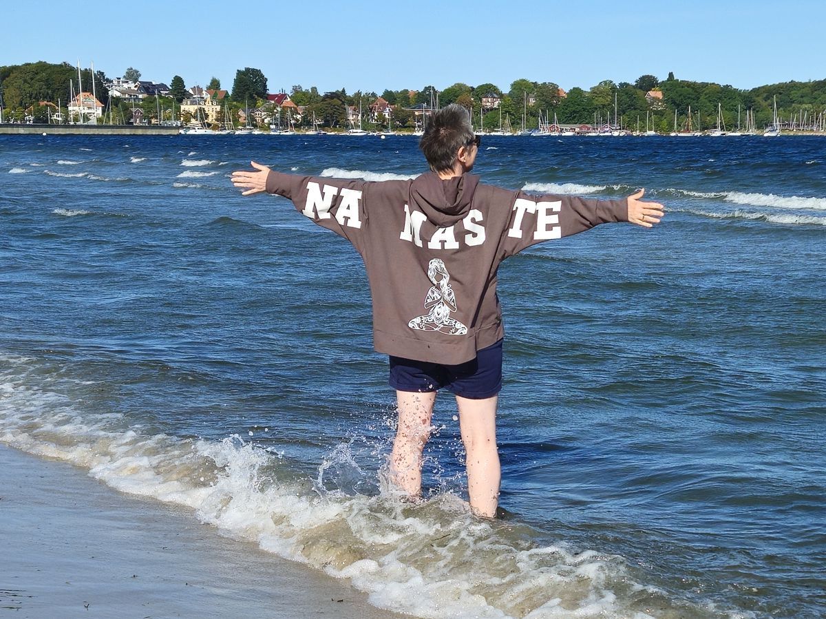 Ines Meyrose - Outfit 2025 - Hoodie braun - Aufdruck NAMASTE - am Strand in Shorts