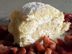 Biskuitrolle mit Limetten-Mascarpone-Füllung, bestäubt mit Puderzucker und garniert mit frischen Erdbeeren