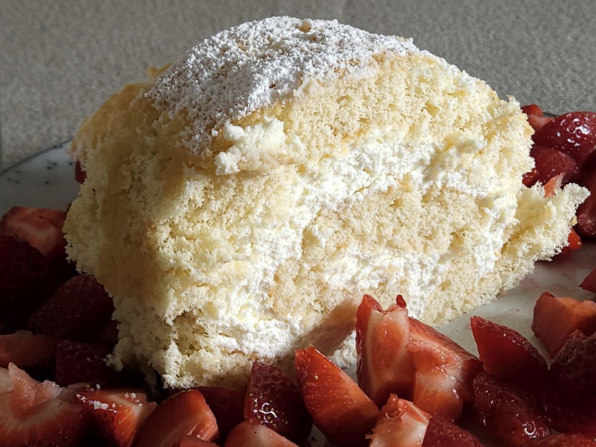 Biskuitrolle mit Limetten-Mascarpone-Füllung, bestäubt mit Puderzucker und garniert mit frischen Erdbeeren