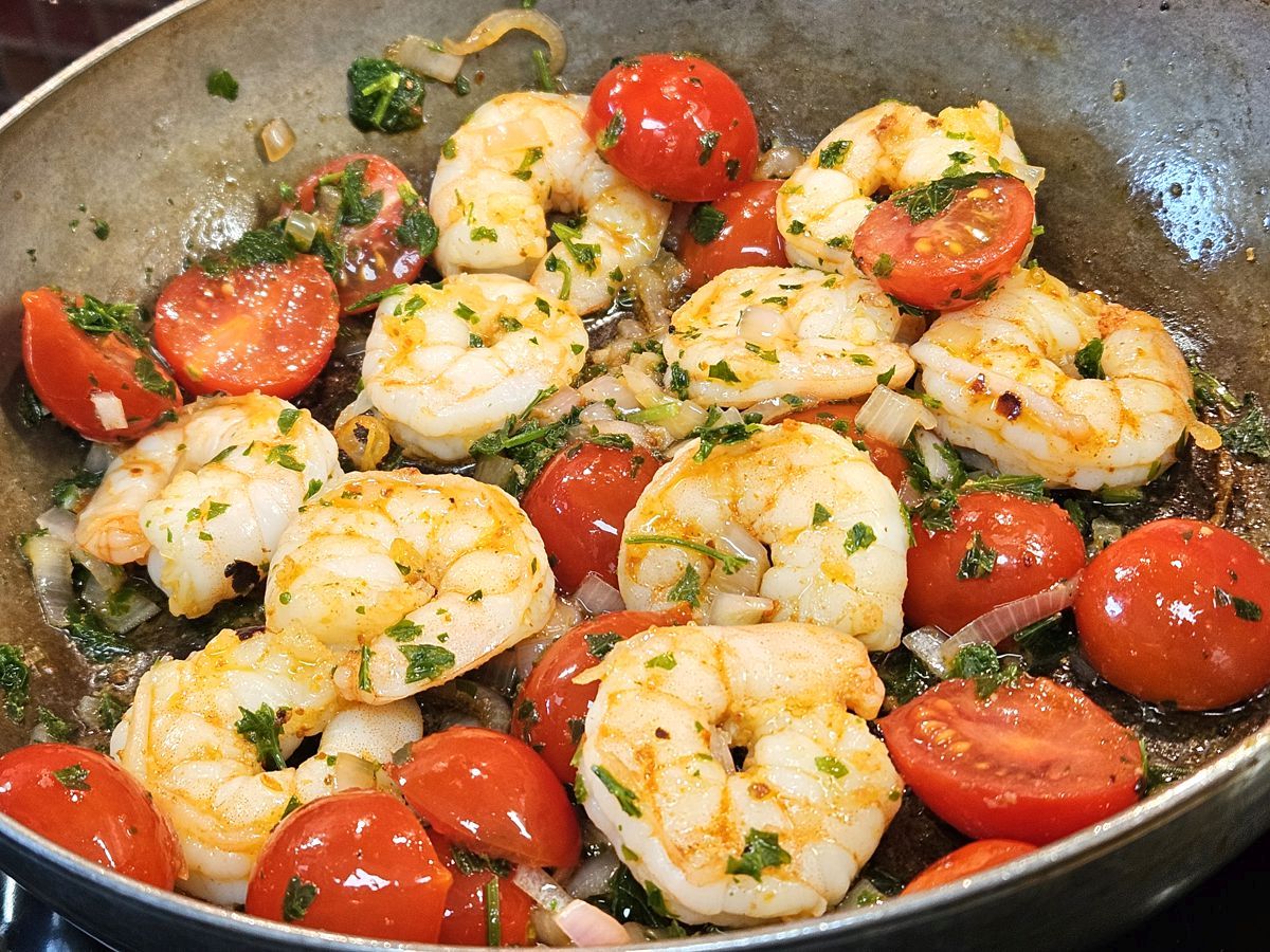 Scampi mit Olivenöl. Harissa, Schalotten, Petersilie, Kirschtomaten in einer Eisenpfanne